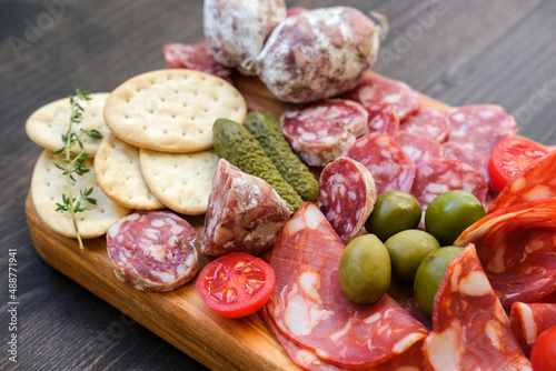 Various types of salami on a wooden board, served with olives, crackers and pickles and cracker. Food for an aperitif and dinner lunch in the restaurant. 