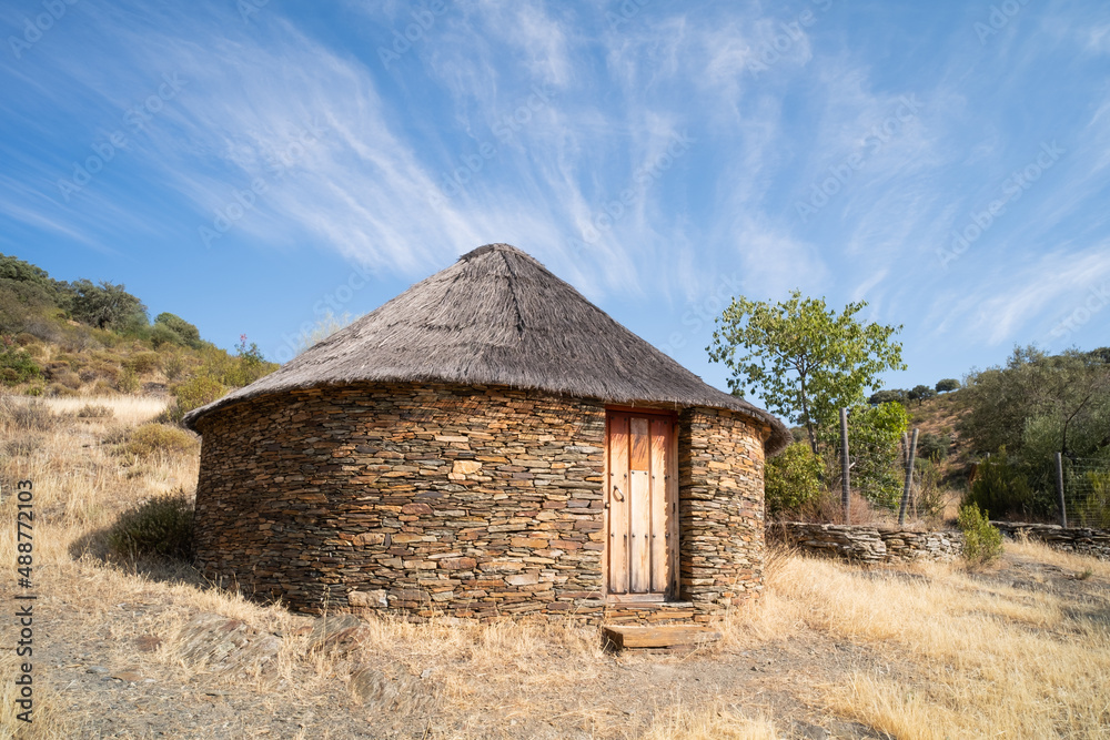 Old cabin or hut with a round shape and slate stone walls and a broom and straw roof