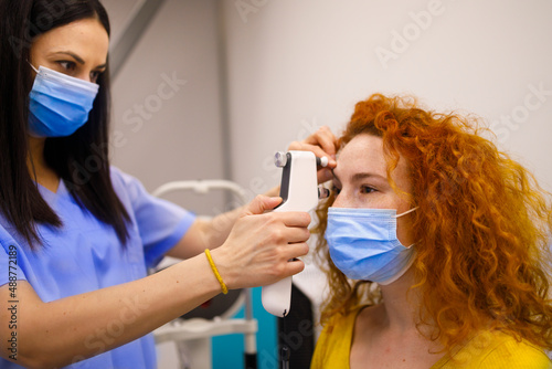 Female doctor with a face-mask examine the eyes of her customer