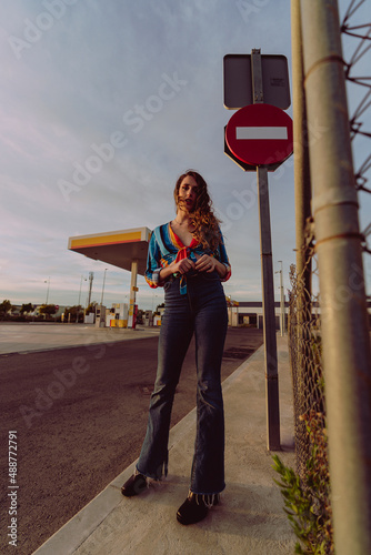 Chica delgada de pelo ondulado poniéndose botas y tomándose fotos en gasolinera