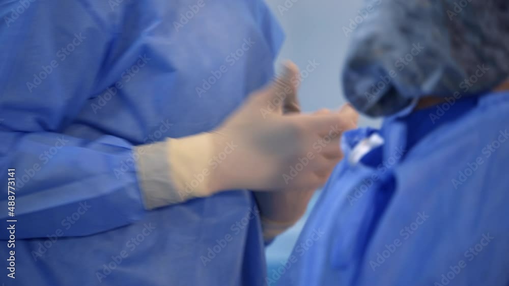 Surgery professional getting ready for operation. Doctor’s hands putting on latex gloves and adjusting them tightly to the fingers. Close up. Surgery professional getting ready for operation. Doctor’s hands putting on latex gloves and adjusting them tightly to the fingers. Close up.