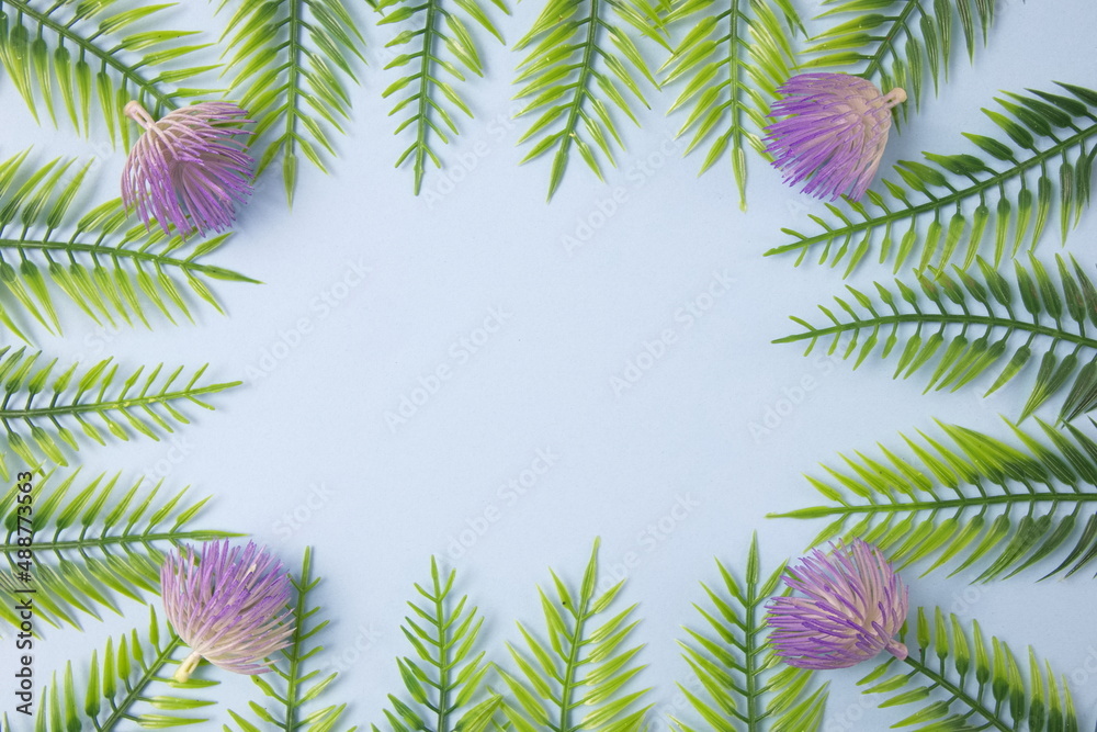 Green leaves with flowers on a light blue background with copy space. Flat lay scene.
