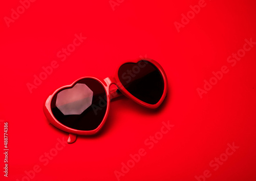 Red heart shaped sunglasses on vibrant red background. Valentines day, Purim, travel concept, banner with a copy space.