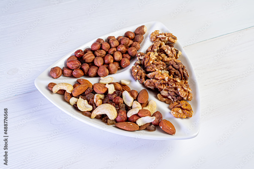 Various nuts close-up on a white plate on a white wooden table. Various nuts close-up on a white plate on a white wooden table.