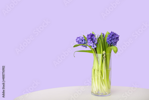 Vase with hyacinth flowers on table against color wall