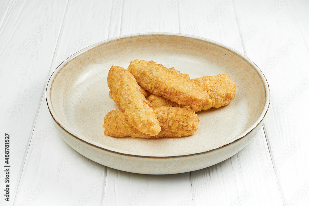 Fried fish fillet in breading on a plate on a white wooden plate Fried fish fillet in breading on a plate on a white wooden plate