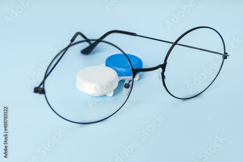 Round glasses for vision and a container with contact lenses on a blue background with a place for text