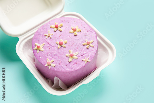 Plastic lunch box with tasty bento cake for International Women's Day celebration on turquoise background, closeup