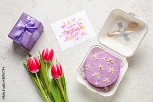 Plastic lunch box with tasty bento cake, greeting card and flowers on light background