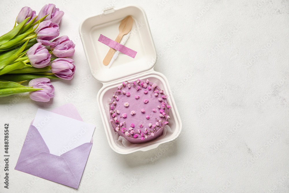 Plastic lunch box with tasty bento cake, envelope and flowers on light background Plastic lunch box with tasty bento cake, envelope and flowers on light background
