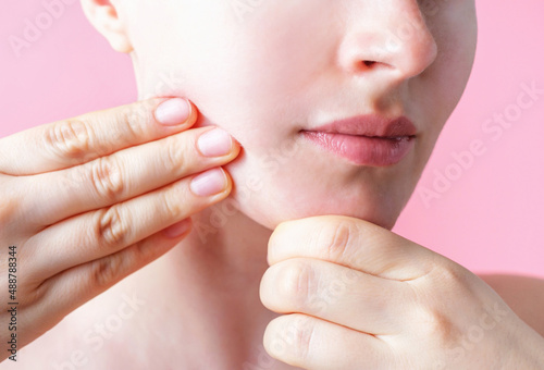 Female hands do self-massage of the face close-up on pink background.