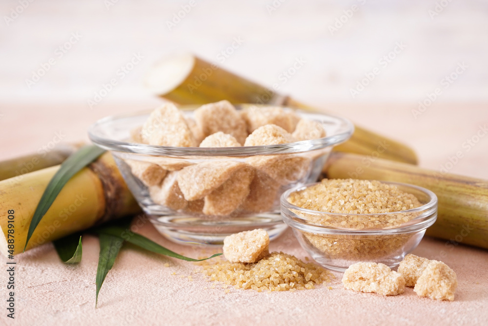 Fototapeta premium Granulated brown sugar, sugarcane and green leaf on a beige background. Close-up.