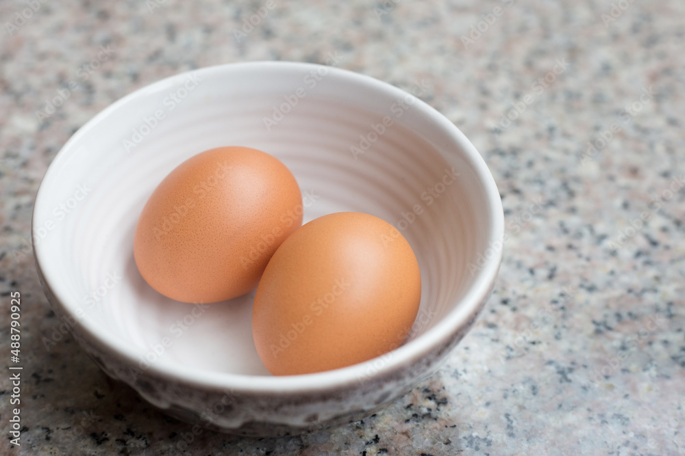 Two fresh light brown eggs in a cup on a granite table. Two fresh light brown eggs in a cup on a granite table.