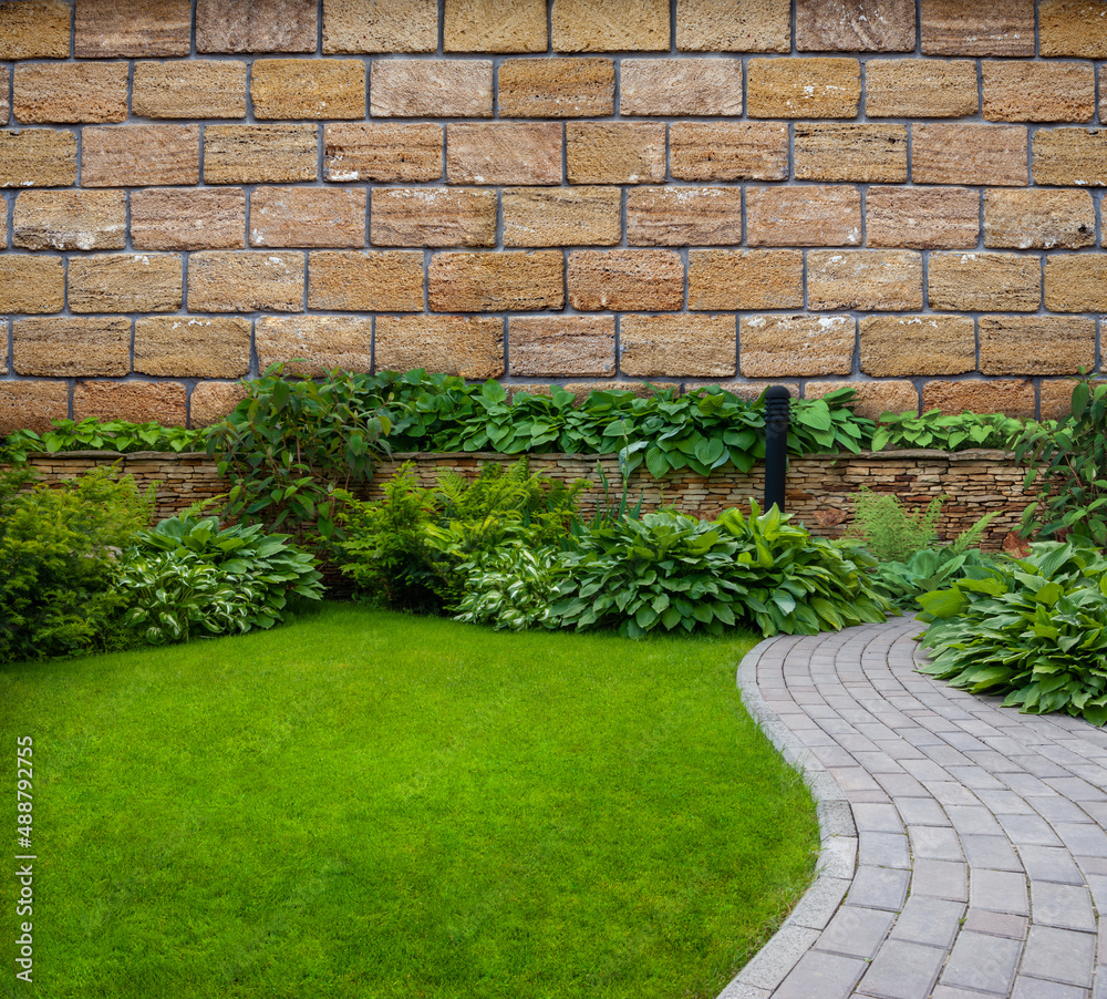 Obraz premium Garden stone path with grass growing between the stones against the backdrop of a stone wall.