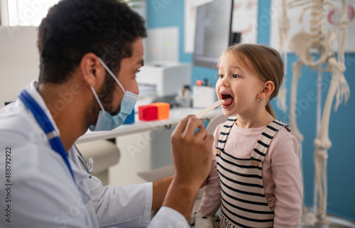 Young male doctor checking little girl's throat in his office.