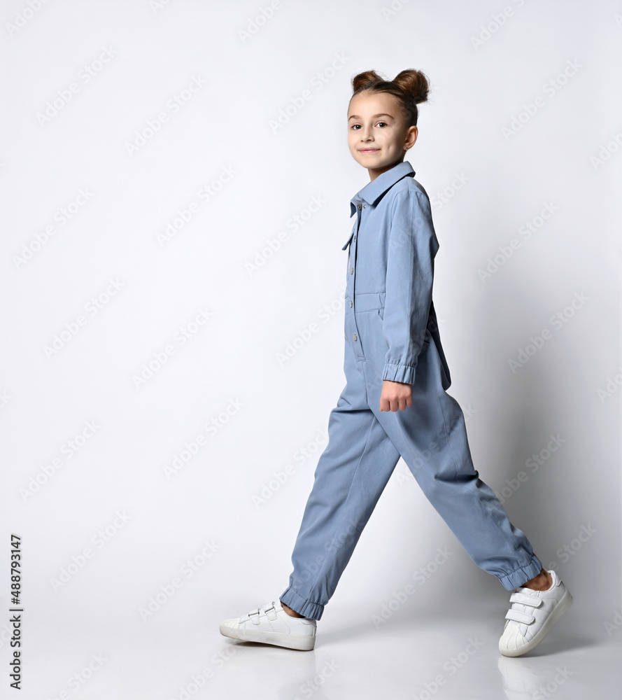 beautiful girl with a bagel hairstyle walking in a blue cotton summer  jumpsuit with comfortable pockets. on a light background. Children's  fashion Stock Photo | Adobe Stock