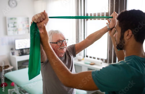 Young physiotherapist exercising with senior patient in a physic room photo