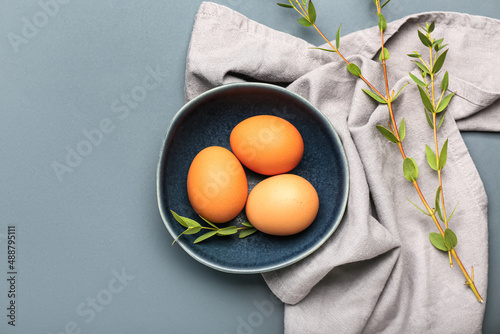Bowl with Easter eggs and green leaves on dark background