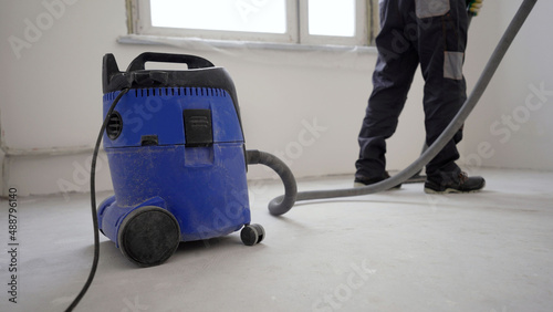 Worker washes the floor with a vacuum cleaner from industrial concrete dust and cement mud during home renovation. A worker vacuums a concrete floor. photo