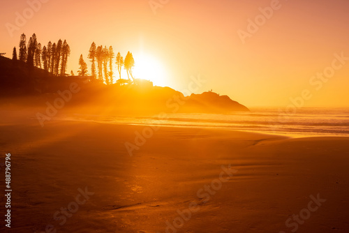 Sunrise on ocean beach with waves and rocks with trees. Joaquina beach in Florianopolis, Brazil