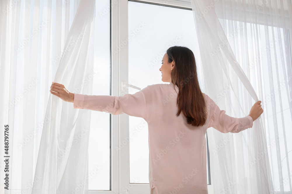 Morning of pretty young woman opening curtains in room Morning of pretty young woman opening curtains in room