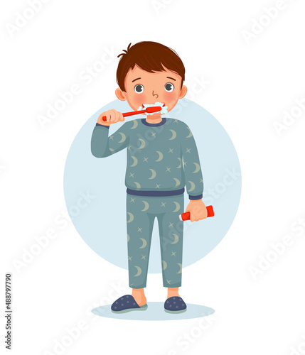 cute little boy in pajamas brushing teeth with toothpaste doing daily routine hygiene activity in bathroom