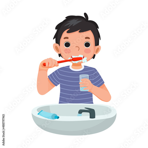 cute little boy brushing teeth with toothpaste holding a glass of water for cleaning daily routine hygiene activity