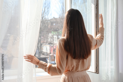 Pretty young woman opening window in room photo