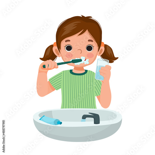cute little girl brushing teeth with toothpaste holding a glass of water for cleaning daily routine hygiene activity