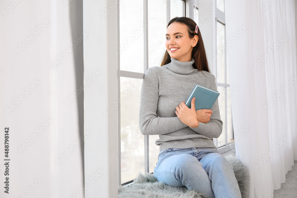 Pretty young woman with book sitting on window sill Pretty young woman with book sitting on window sill