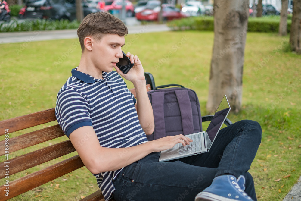 Young caucasian man sitting on the bench, working on the laptop and making Young caucasian man sitting on the bench, working on the laptop and making