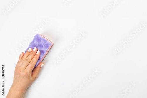 Housewife's hand holds a sponge for cleaning agent on a gray background. Detergent for various surfaces in the kitchen, bathroom and other rooms. Close-up.