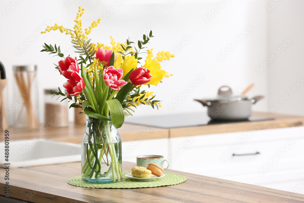 Vase with beautiful flowers, macarons and cup of coffee on kitchen counter Vase with beautiful flowers, macarons and cup of coffee on kitchen counter