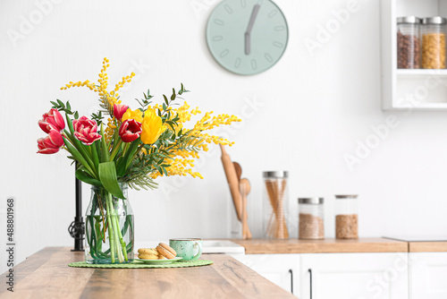 Vase with beautiful flowers, macarons and cup of coffee on kitchen counter