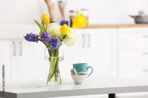 Beautiful flowers, bowl with macarons and cup on dining table in kitchen