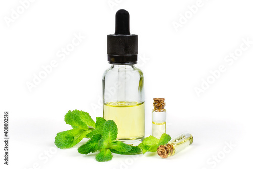 Essential oil of fragrant mint  peppermint  in a transparent glass bottle with a pipette on a white insulated background. Aromatherapy  anti-fatigue  relaxation   spa  skin care.