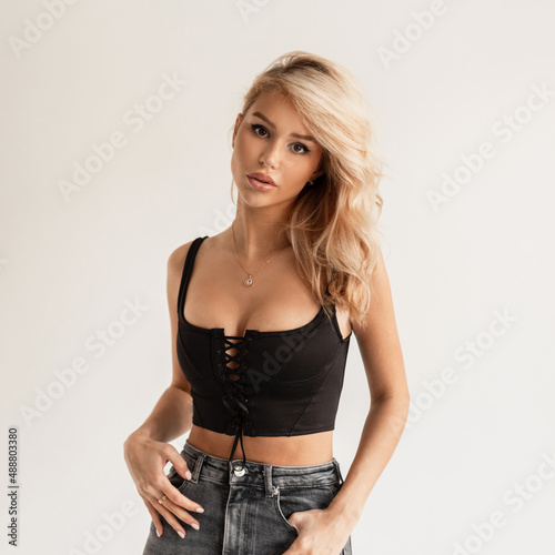 Sexy beautiful glamorous young blonde woman in a black bustier top and High waisted jeans posing in the studio on a white background photo