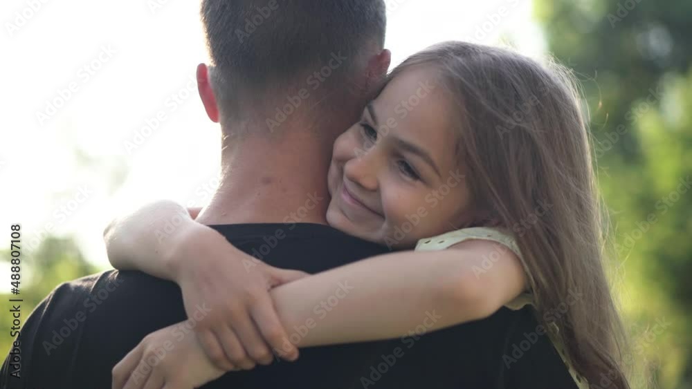 Portrait of happy girl hugging man outdoors in summer spring park looking away. Brunette Caucasian daughter with brown eyes embracing parent enjoying weekend leisure outdoors Portrait of happy girl hugging man outdoors in summer spring park looking away. Brunette Caucasian daughter with brown eyes embracing parent enjoying weekend leisure outdoors