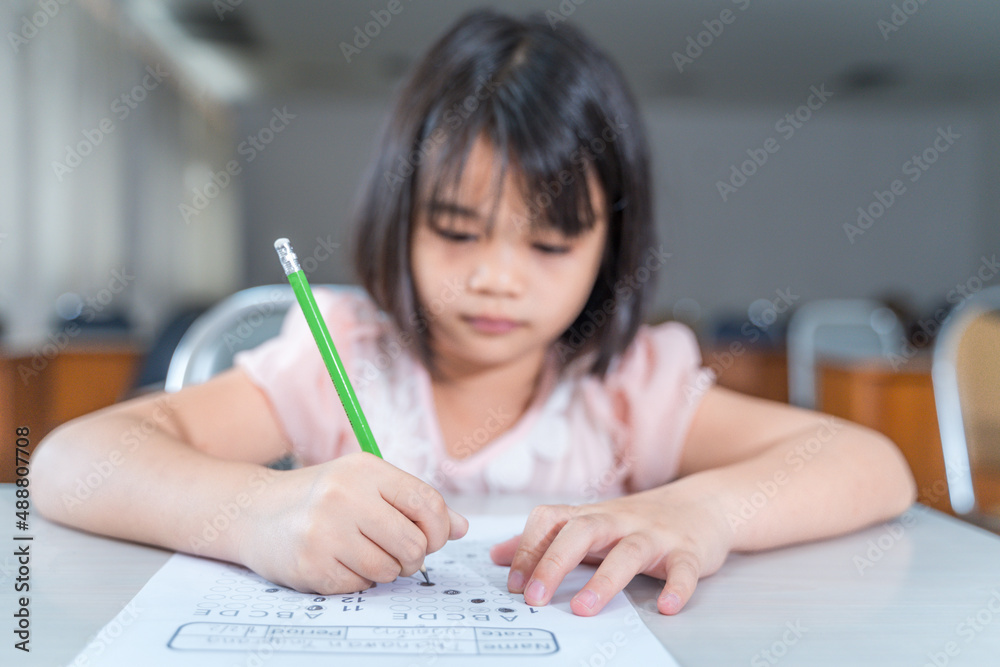 A female Asian kid student concentrate writing on the examination paper in the class