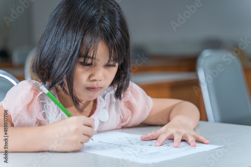 A female Asian kid student concentrate writing on the examination paper in the class