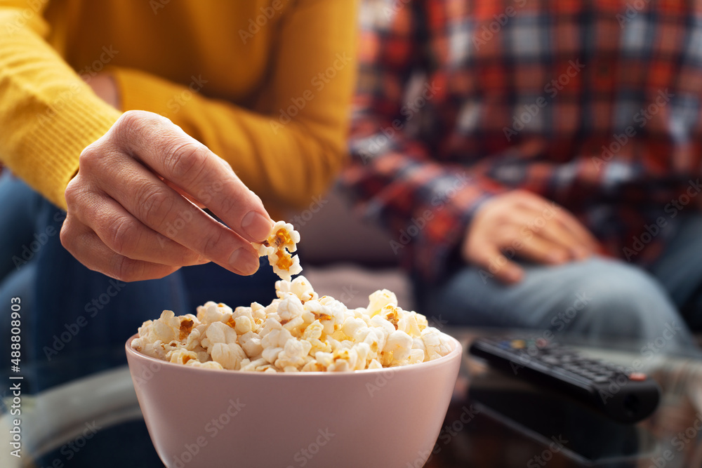 Caucasian couple sitting on sofa with popcorn and tv remote