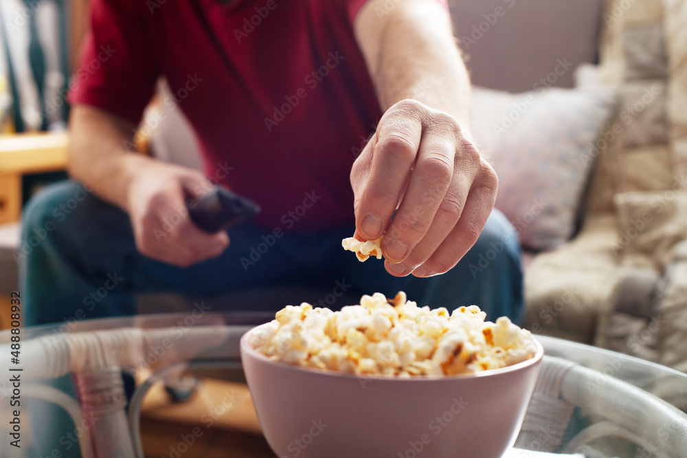 Caucasian man sitting on sofa with popcorn and tv remote
