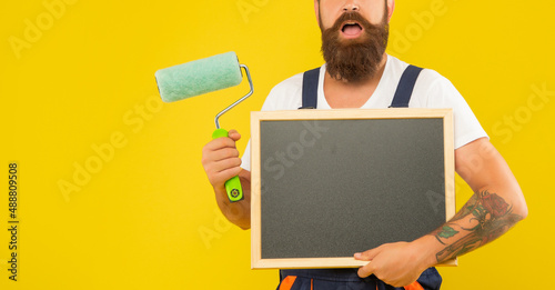 Foto cropped man renovator hold paint roller and blackboard with copy space on yellow