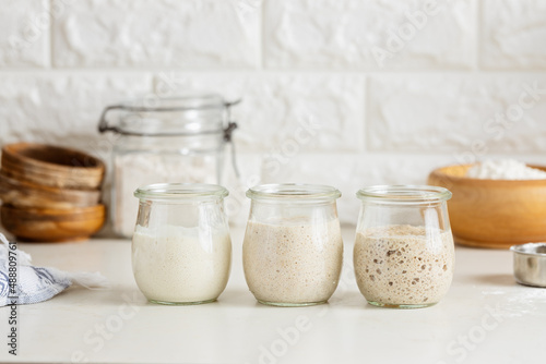 Three glass jars with active sourdough starter. Spelt, rye, and wheat. photo