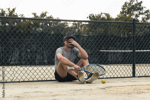 Tired tennis player sits on the court, losses in sports , failure emotions of sportsman. photo