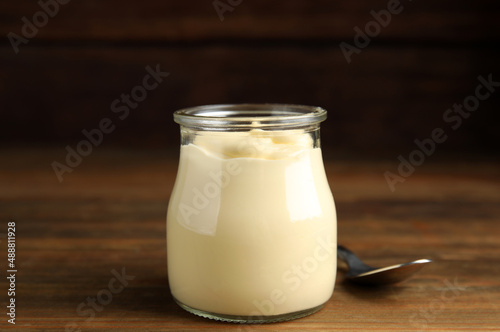 Jar of delicious mayonnaise and spoon on wooden table