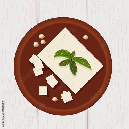 Tofu on wooden plate with soya beans and basil leaves top view
