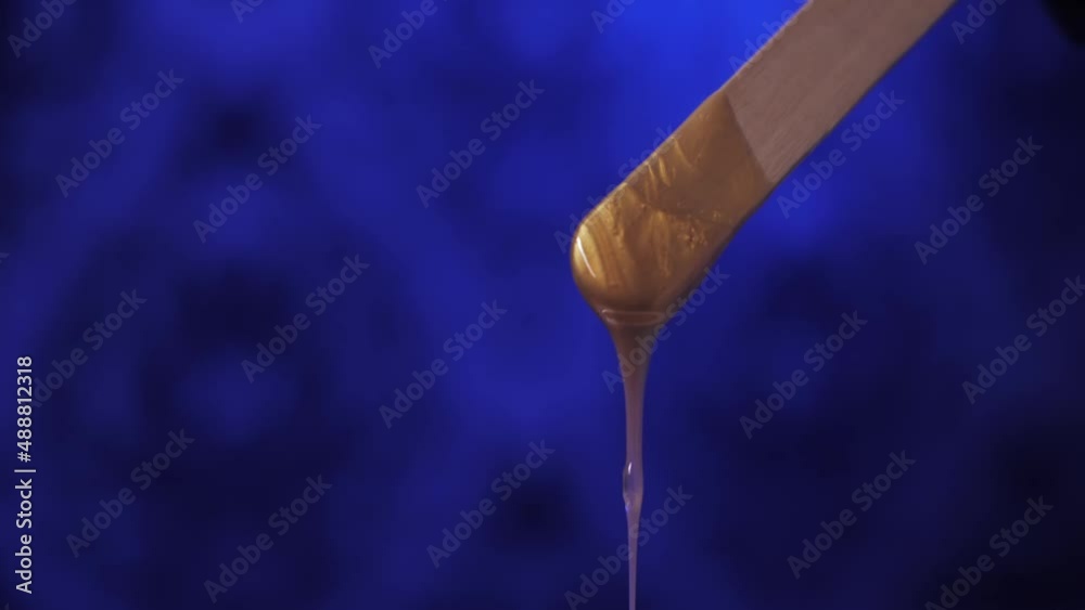 Sugar paste for sugaring flows down from a wooden spatula. Hair removal, epilation, depilation, beauty. Sugar paste for sugaring flows down from a wooden spatula. Hair removal, epilation, depilation, beauty.