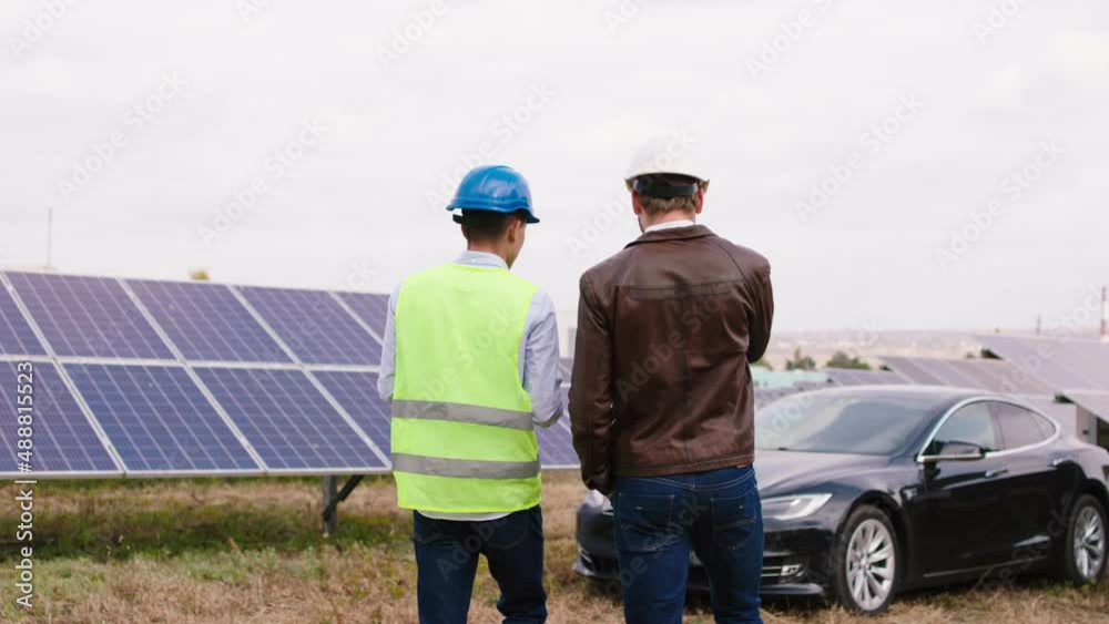 Concept of modern solar panels two ecological engineers walking through the large photovoltaic batteries they discussing together using digital tablet and wearing protective helmets Concept of modern solar panels two ecological engineers walking through the large photovoltaic batteries they discussing together using digital tablet and wearing protective helmets