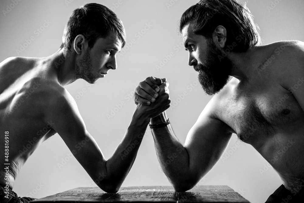 Heavily muscled bearded man arm wrestling a puny weak man. Arms